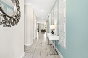 A hallway with a white tiled floor, a white sink with a black lamp, and a decorative mirror on the left. - 2779 Oxymoron Way (Kissimmee)