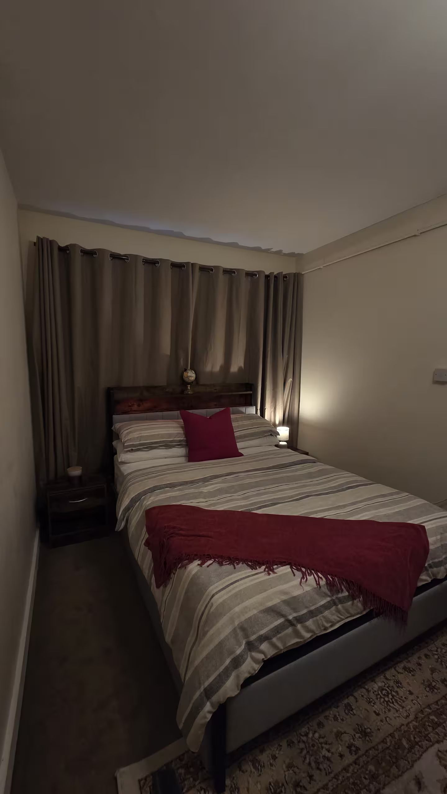 Un lit simple avec une tête de lit, une table de chevet avec une lampe et un tapis à motifs.