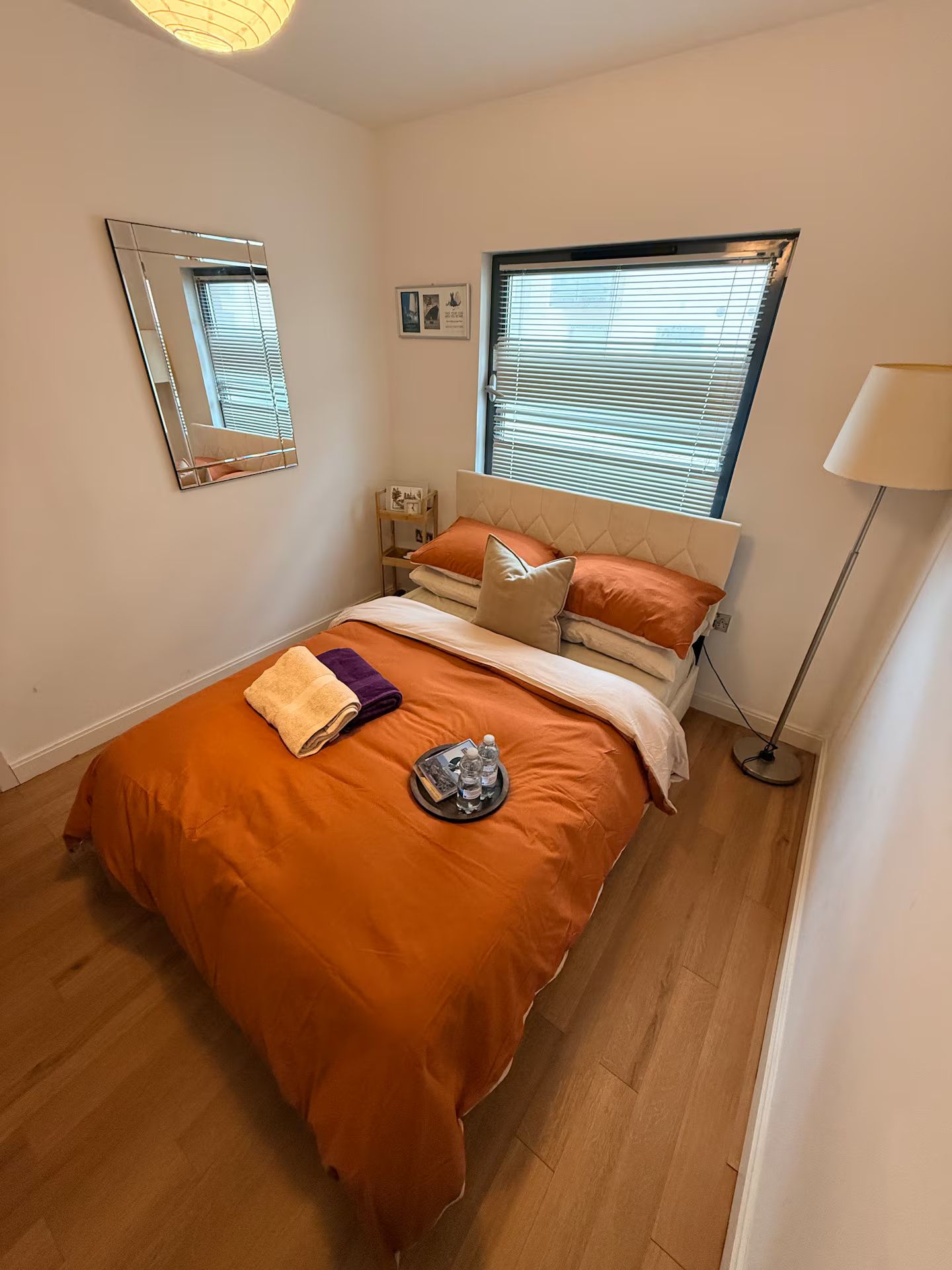 A bedroom with a bed, a bedside table, a lamp, and a window with blinds.
