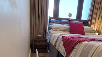 Un dormitorio con cama, radiador, ventana con cortinas y una alfombra estampada.