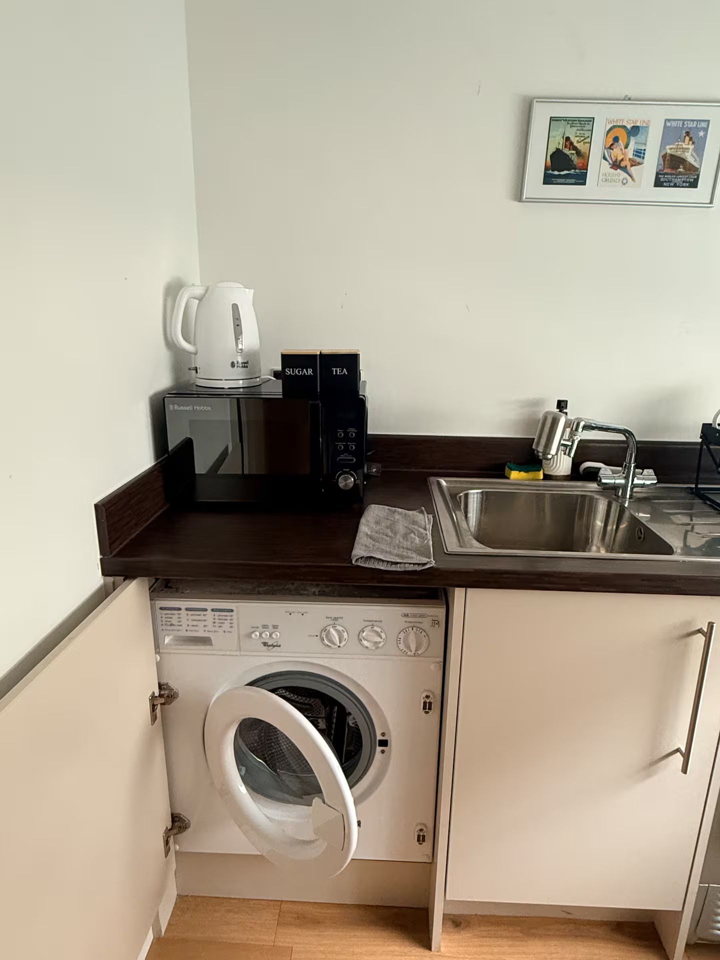 Eine kleine Küchenzeile mit Mikrowelle, Kaffeemaschine, Spüle und integriertem Waschtrockner.