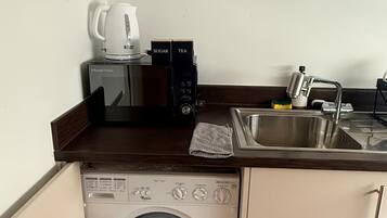 Eine kleine Küchenzeile mit Mikrowelle, Kaffeemaschine, Spüle und integriertem Waschtrockner.