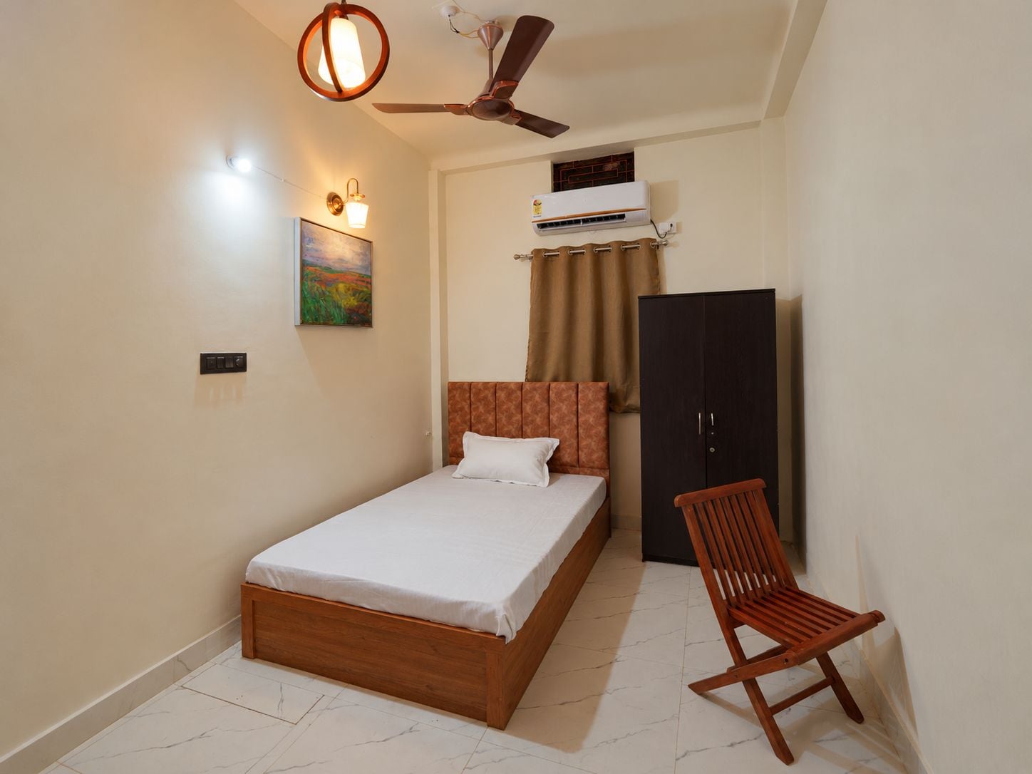 A bedroom with a bed, a chair, a wardrobe, a ceiling fan, and an air conditioning unit.