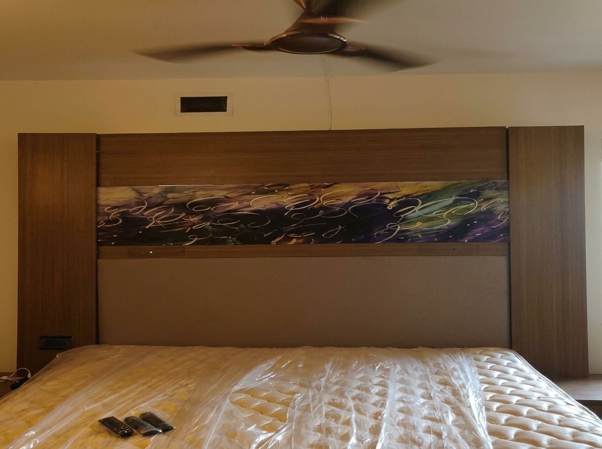 Une chambre d’hôtel avec un lit, un ventilateur de plafond et un grand tableau abstrait accroché au-dessus de la tête de lit.