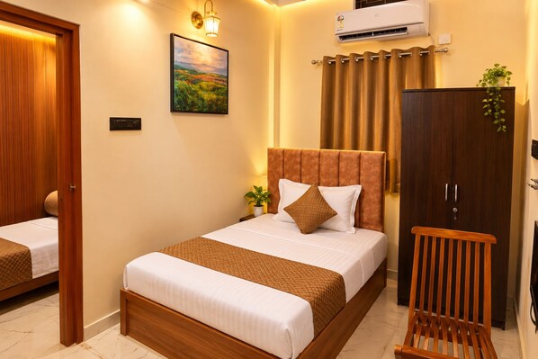A hotel room with a bed, a wardrobe, a nightstand, a lamp, and an air conditioning unit. - Hotel Shree Kripa (Ujjain)