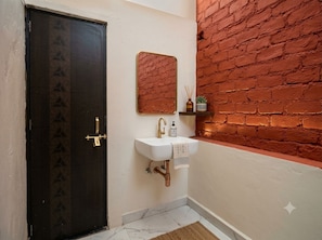 Un baño con puerta oscura, un lavabo blanco con grifo dorado, un espejo y una pared de ladrillo.