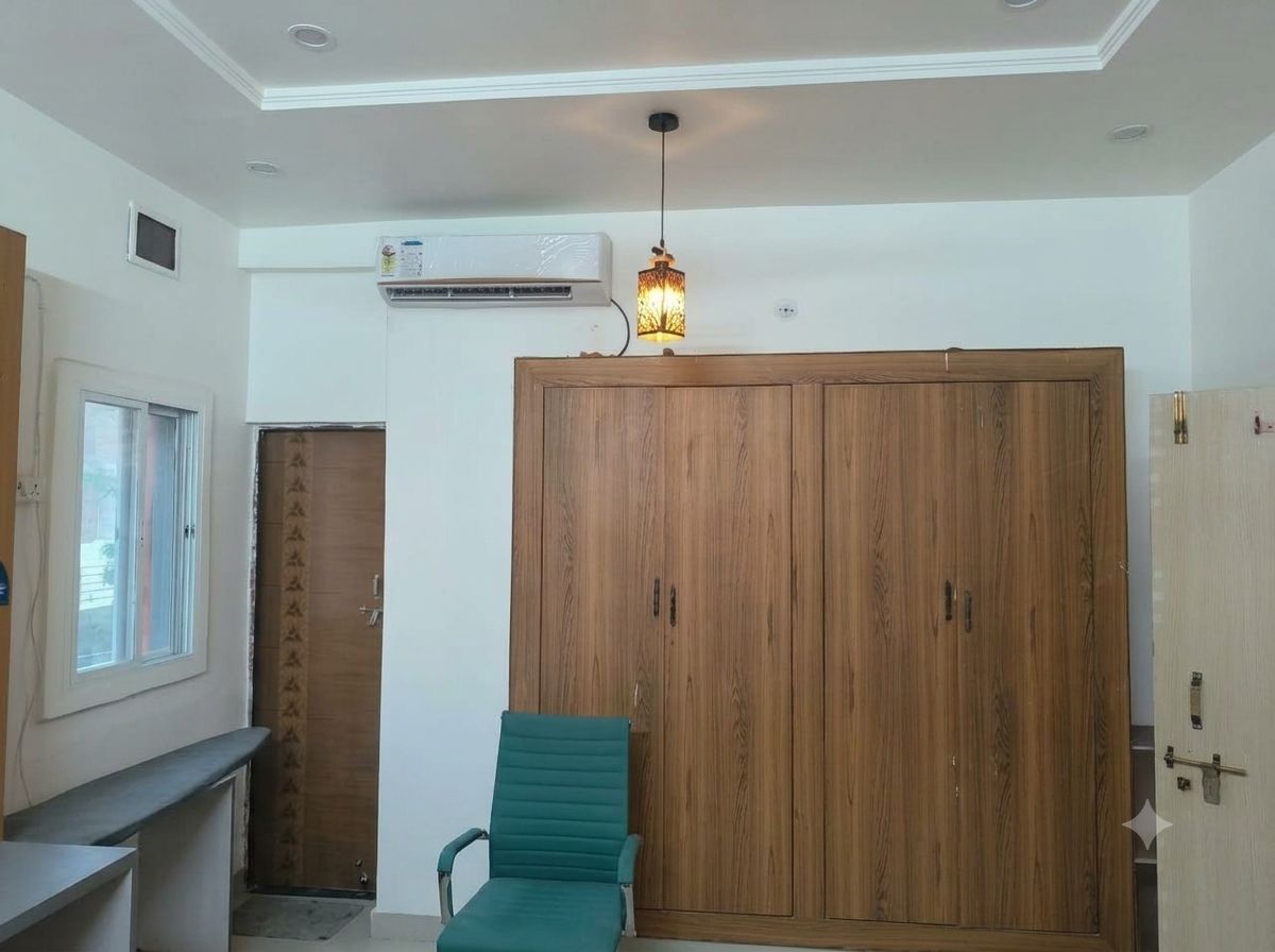 Une pièce avec une armoire en bois, une chaise verte et un luminaire fixé au plafond.