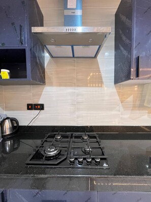 Una cocina con estufa a gas, hervidor y campana extractora azul.