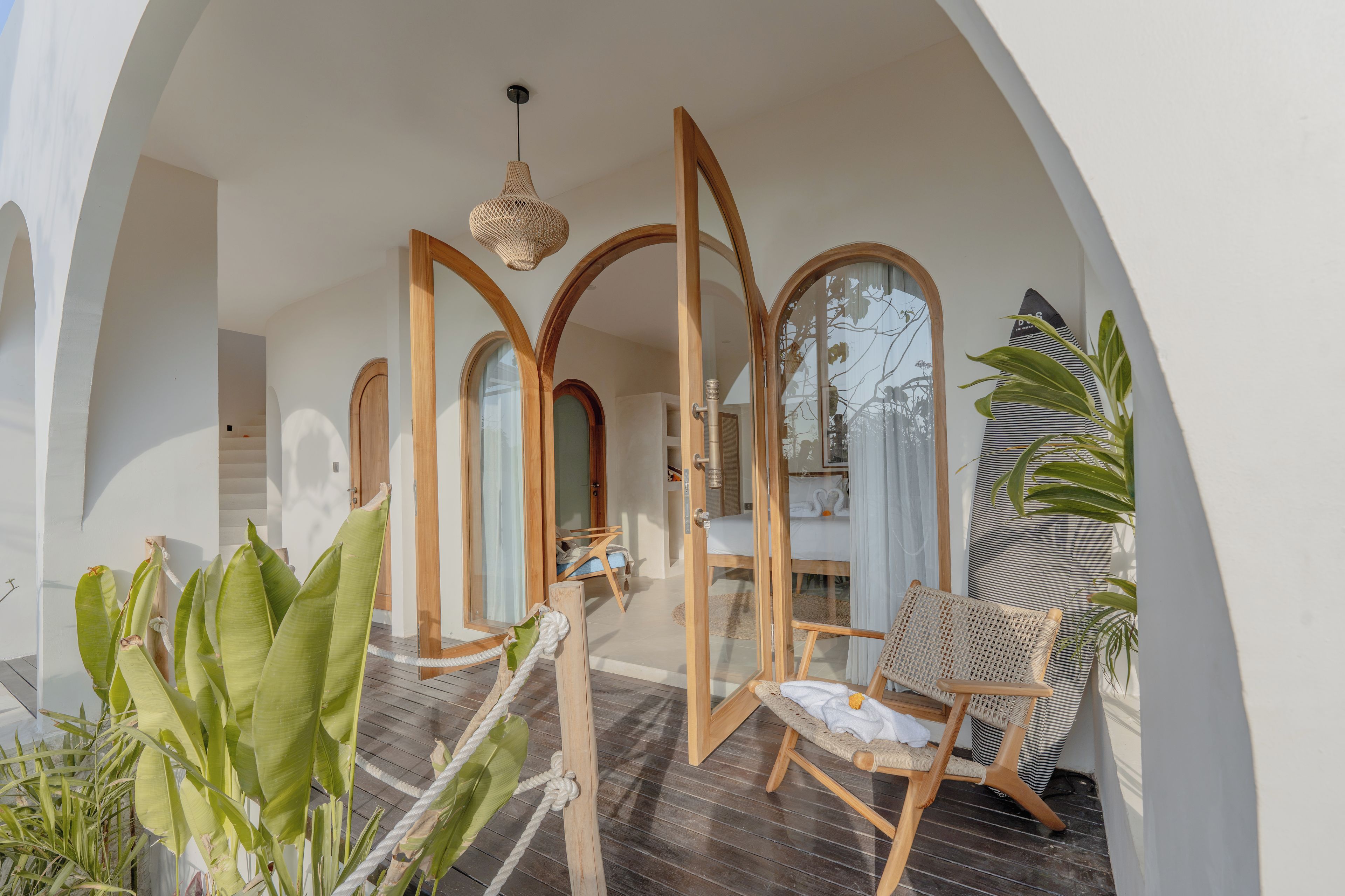 A room with a wooden door, a bed, a chair, and a hanging light fixture.