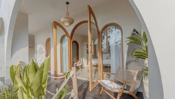 A room with a wooden door, a bed, a chair, and a hanging light fixture.