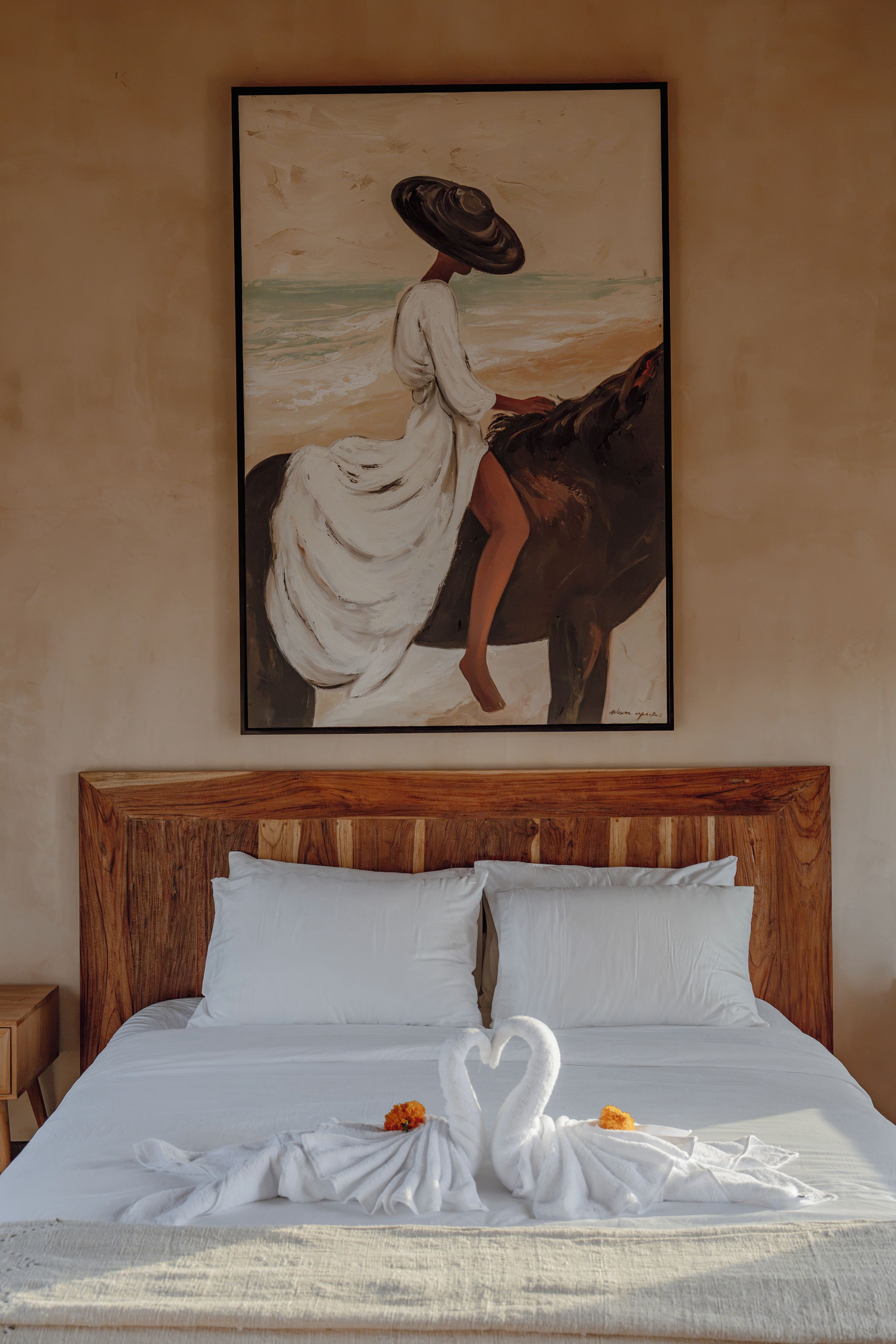 A bedroom with a wooden headboard, a bed with white bedding, and a painting of a woman on a horse.