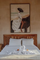 Un dormitorio con cabecera de madera, cama con ropa de cama blanca y un cuadro de una mujer a caballo.