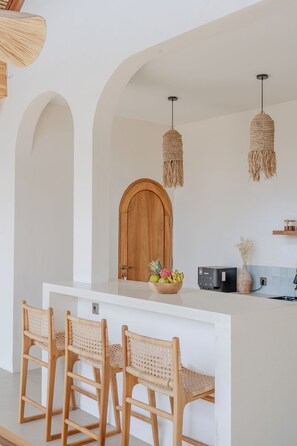 A kitchen with a central island, wooden chairs, and a hanging light fixture. - Aksaya Boutique Hotel - Uluwatu (Badung)
