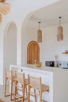 A kitchen with a central island, wooden chairs, and a hanging light fixture.
