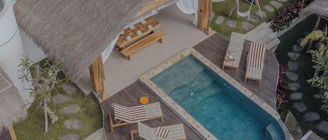 A resort with a swimming pool, lounge chairs, and a thatched-roof structure.