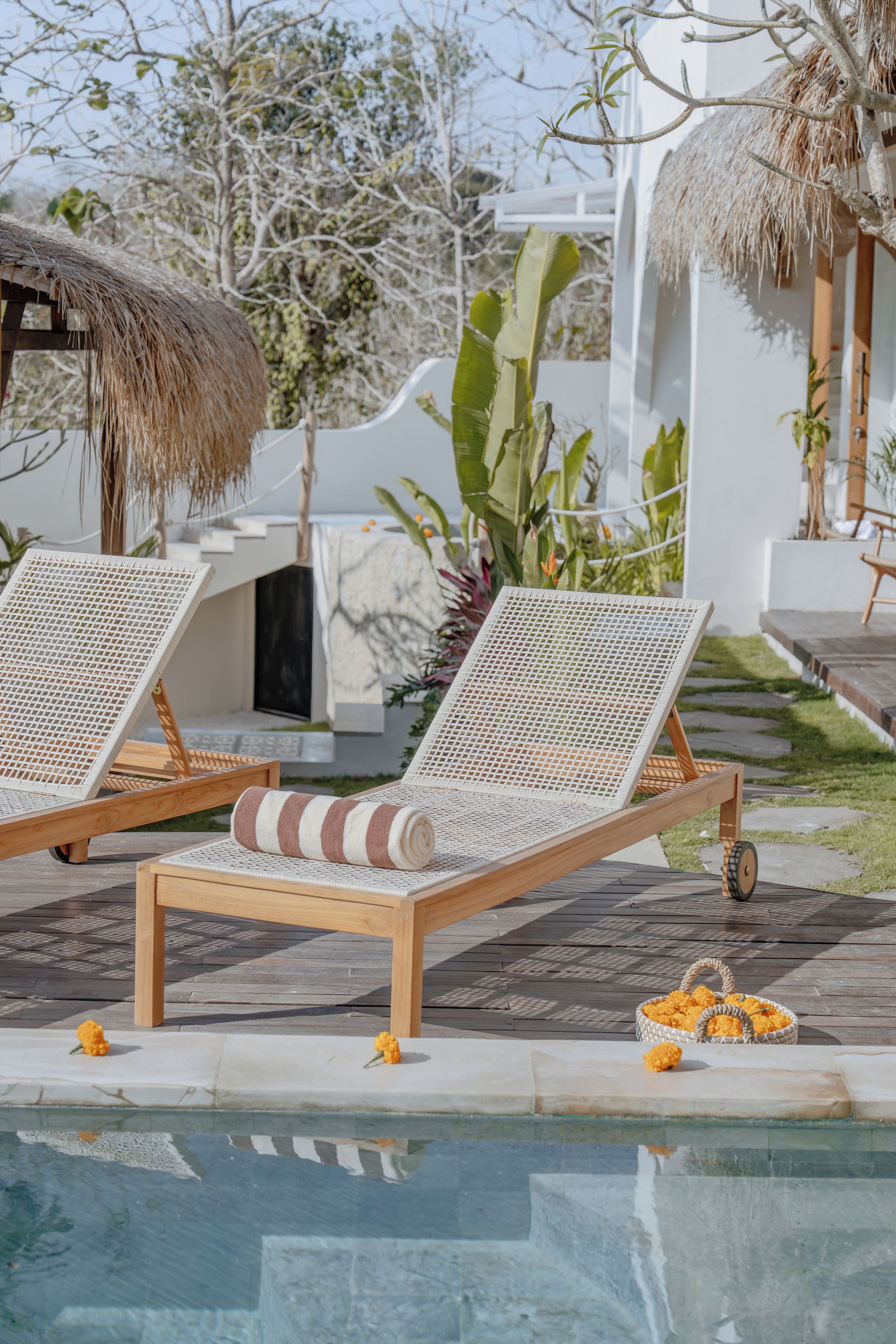 Dos sillones de relax con asiento y respaldo de mimbre, ubicados en una terraza de madera con una piscina al frente.