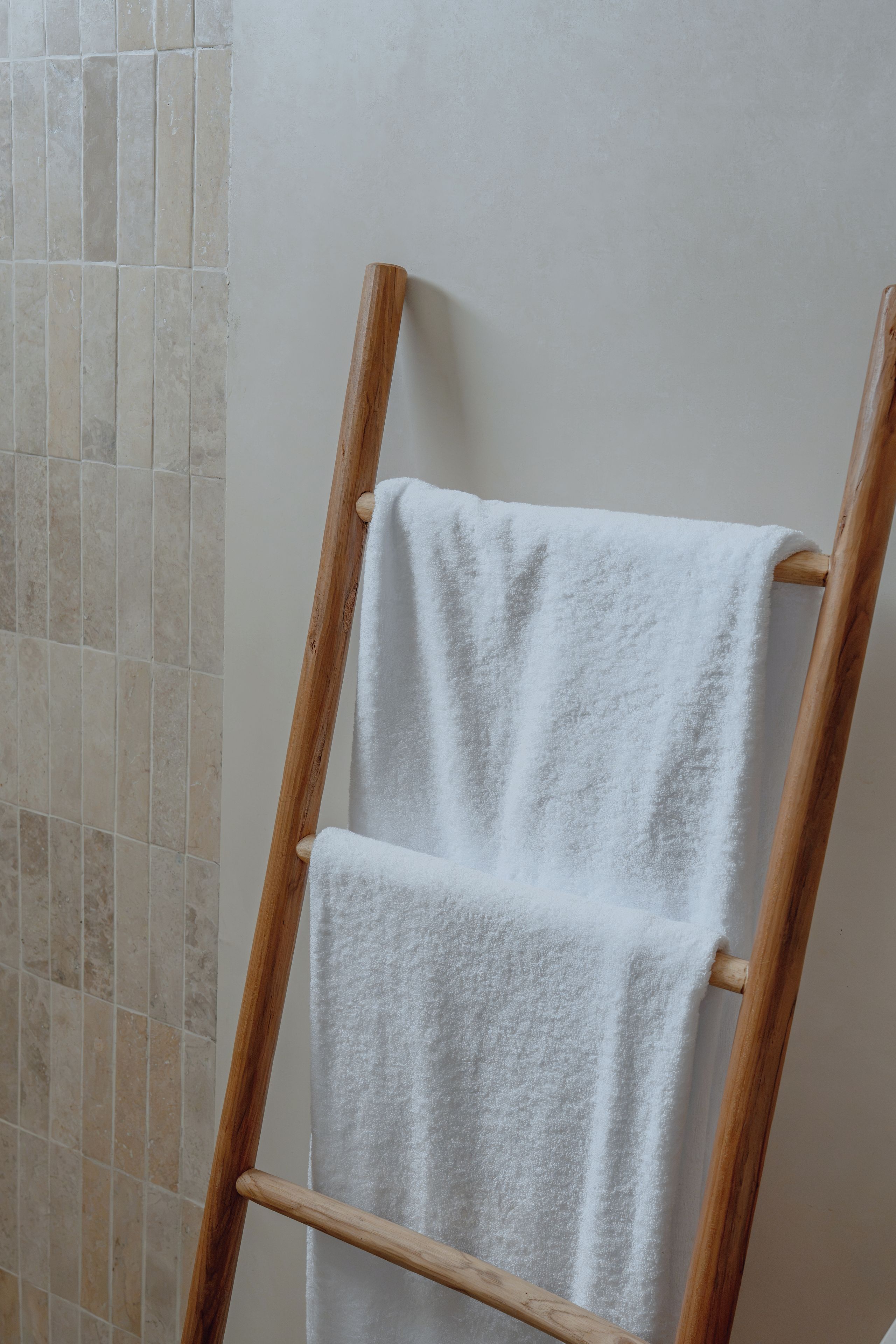 A wooden towel rack with two white towels against a wall with a tiled backsplash.