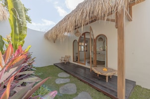 A modern outdoor area with a wooden deck, a thatched roof structure, and a seating area with a table and chairs.
