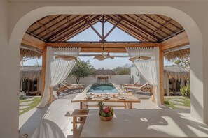 Un espace extérieur abrité, aménagé pour les repas, avec une piscine, du mobilier en bois et une table dressée pour un repas.