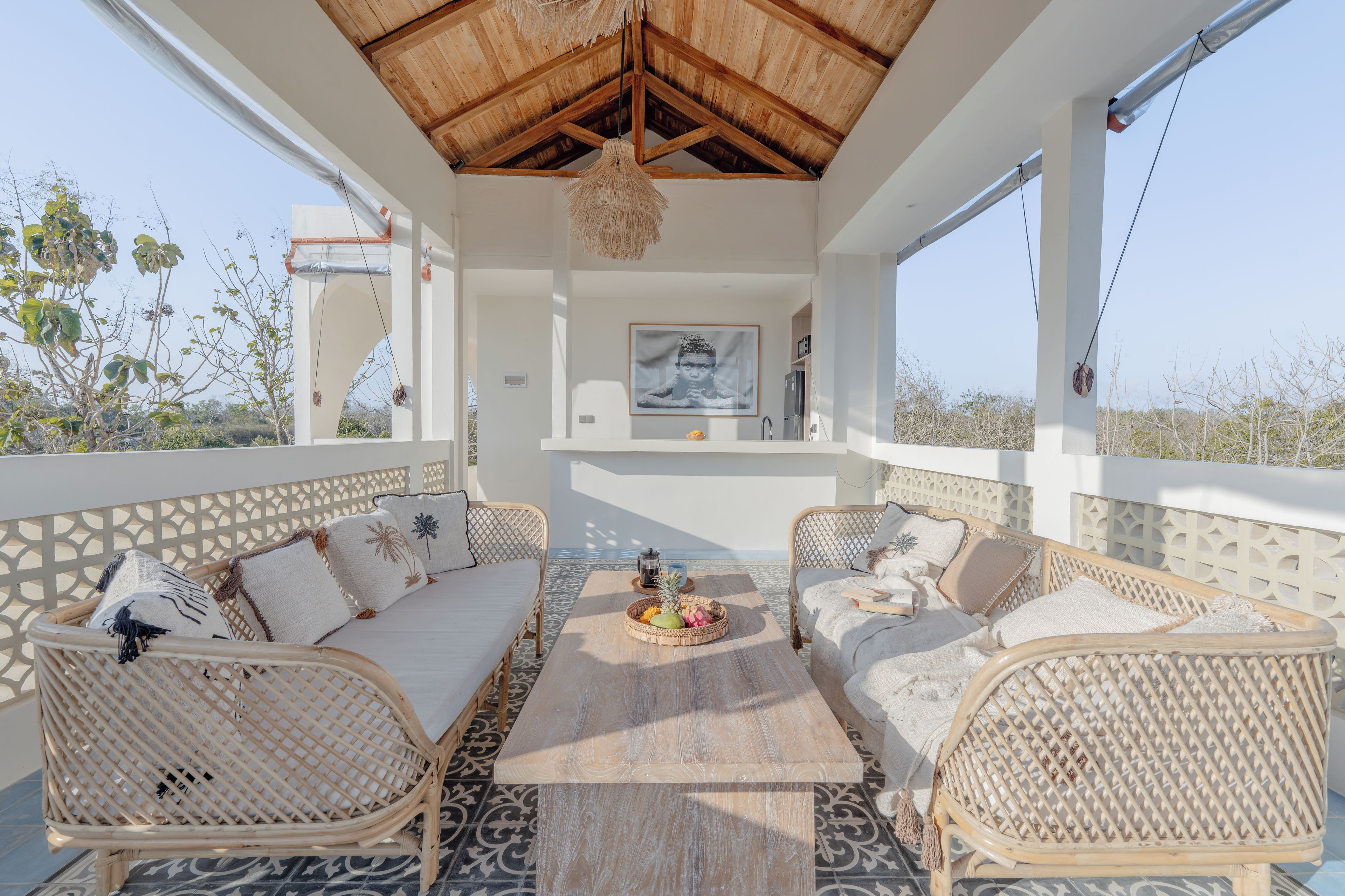 Un espacio de estar al aire libre con luz solar, muebles de mimbre, una mesa de centro de madera y vistas del paisaje circundante.
