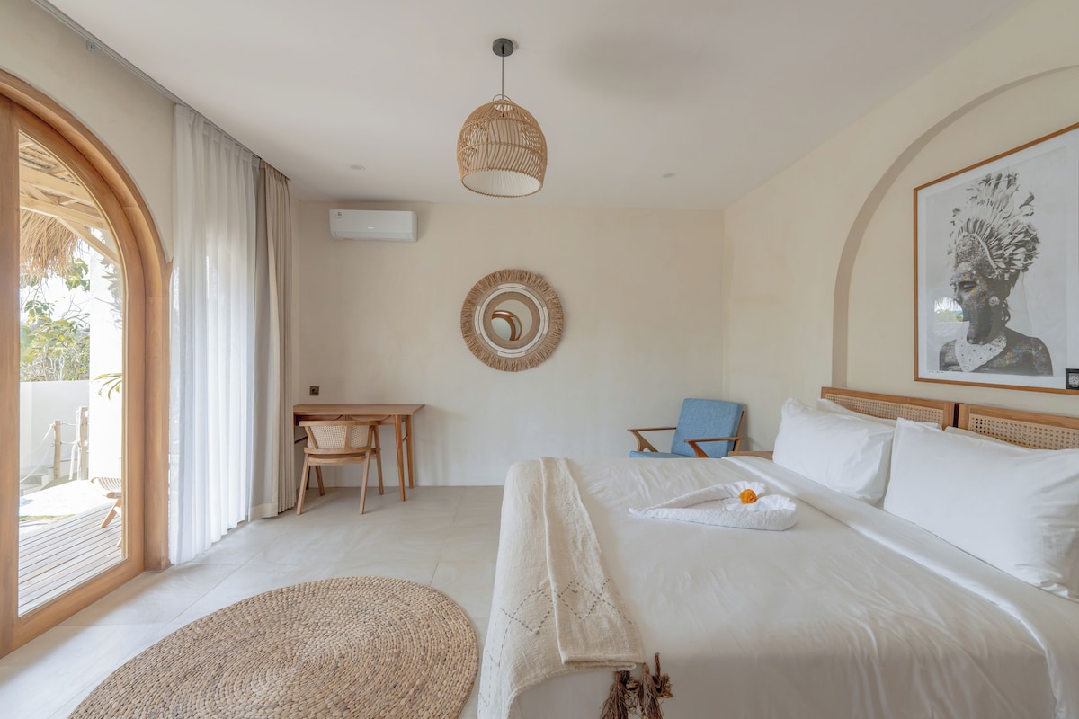 Une chambre à coucher comprenant un lit, un bureau, une chaise, un miroir rond et un luminaire suspendu.