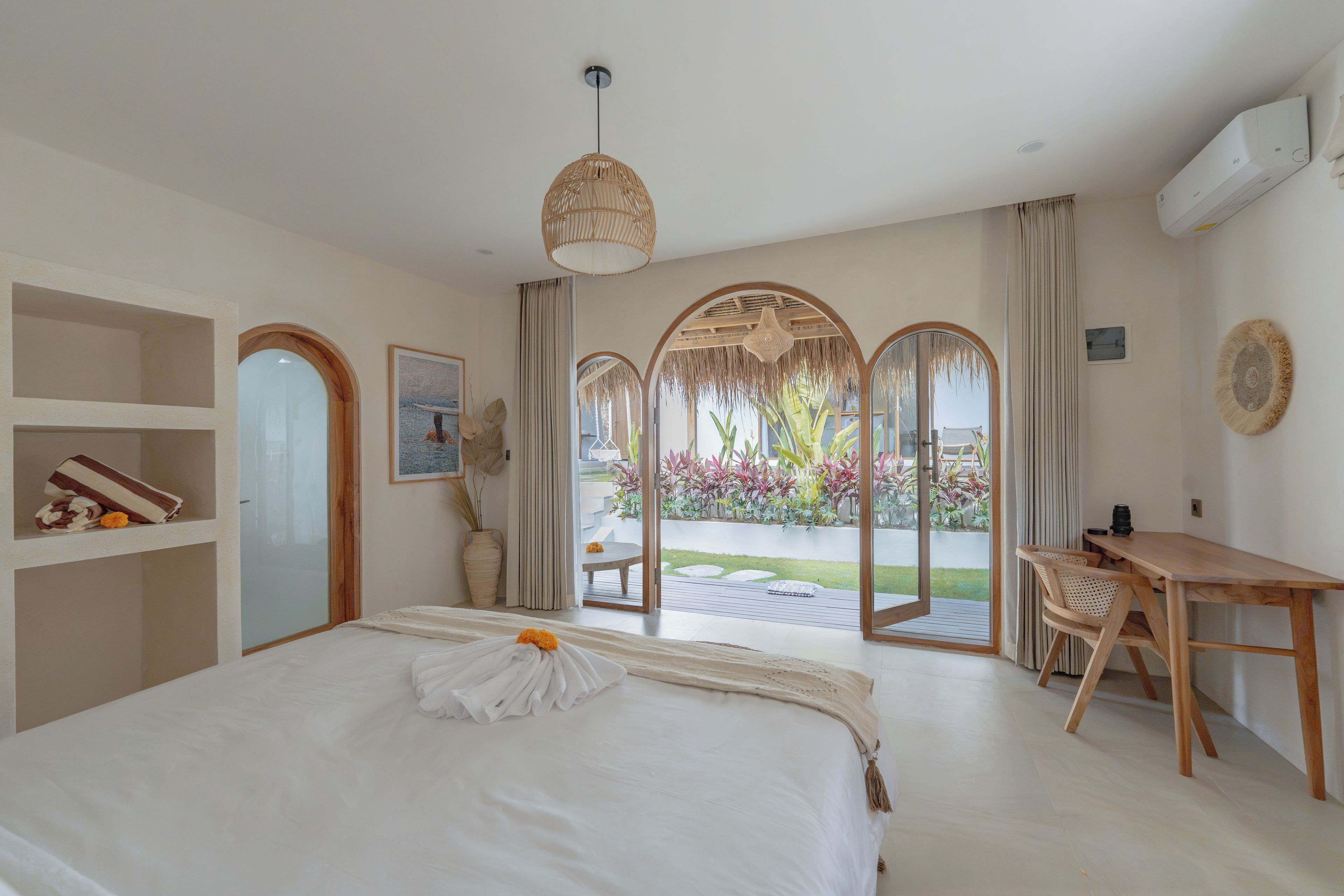 Habitación de hotel con cama, escritorio y vistas a un jardín a través de un ventanal.
