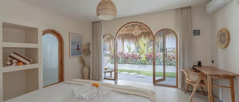 Habitación de hotel con cama, escritorio y vistas a un jardín a través de un ventanal.