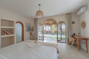 A hotel room with a bed, a desk, and a view of a garden through a glass door.
