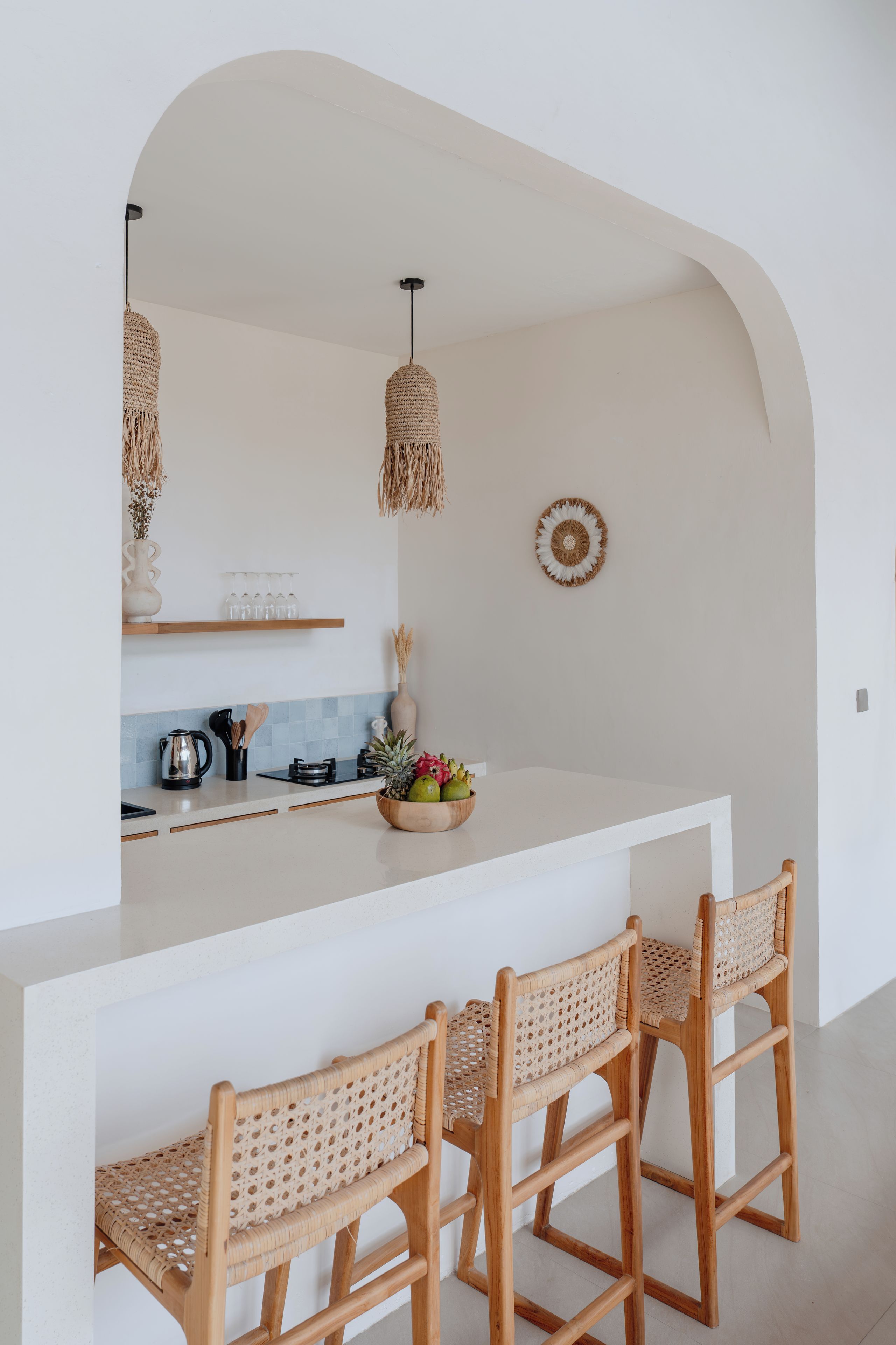Een keuken met een wit eiland, twee barkrukken, hangende lampen en een decoratief bord aan de muur.