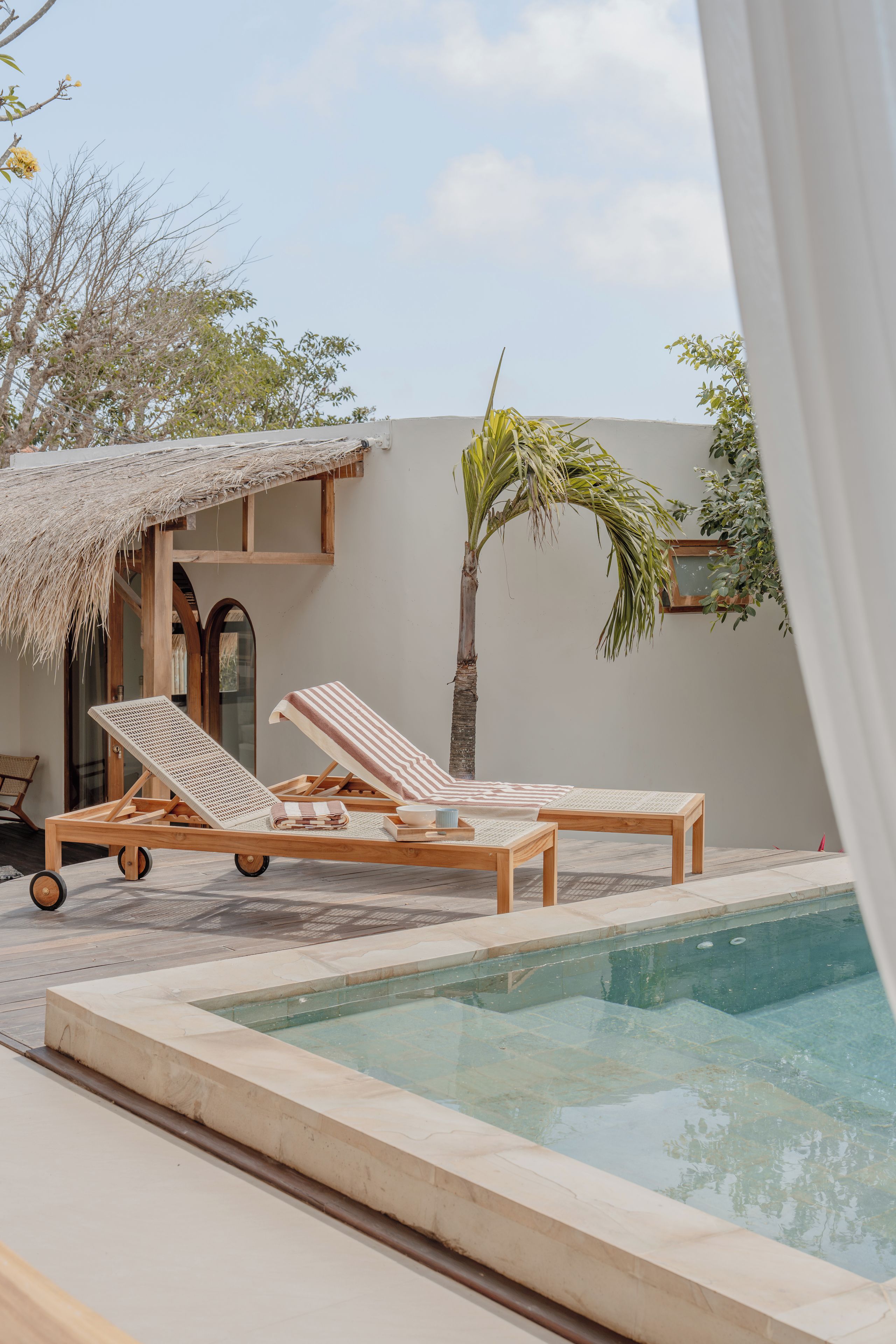 A poolside area with two lounge chairs, a small table, and a thatched-roof structure.