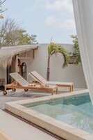 A poolside area with two lounge chairs, a small table, and a thatched-roof structure.