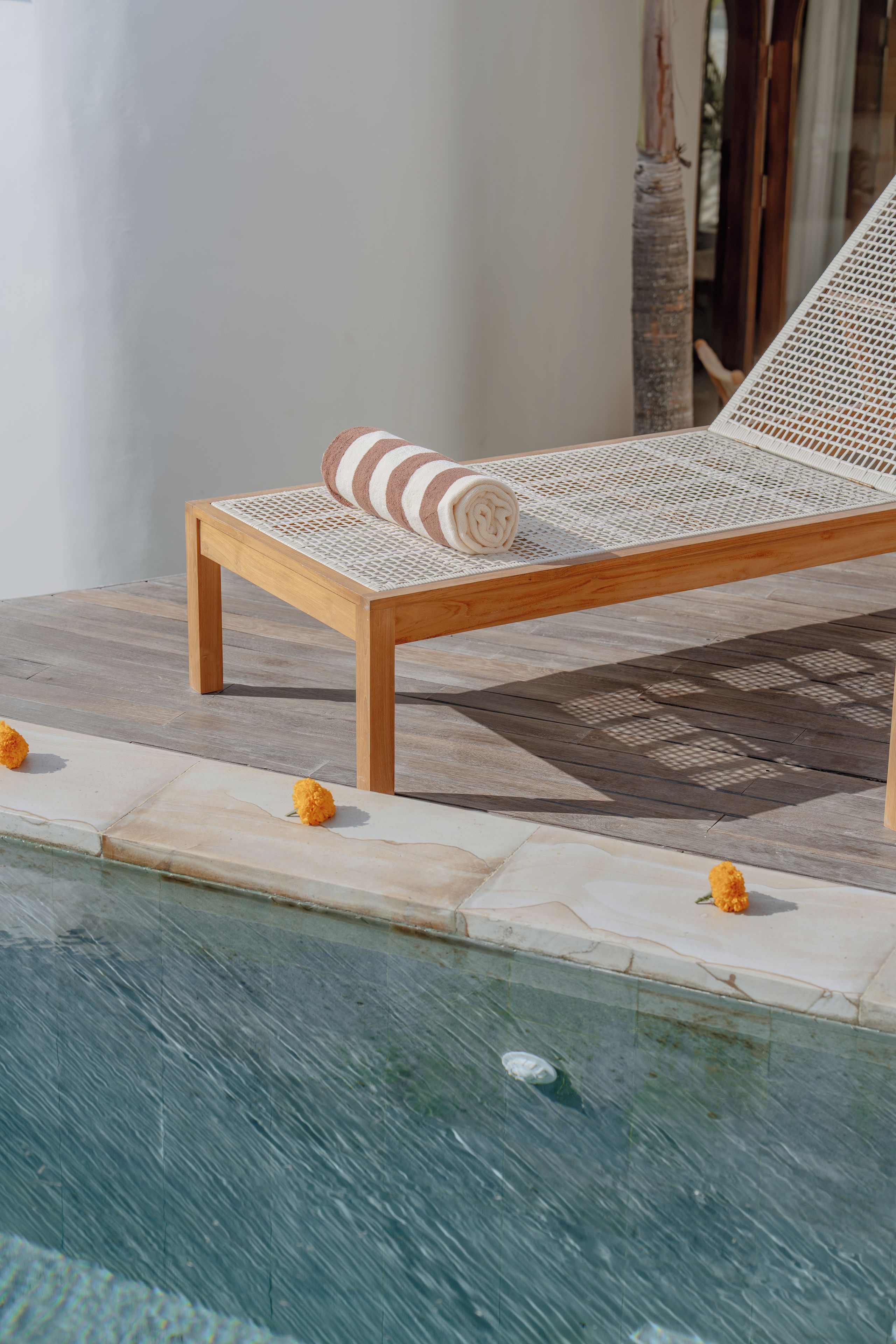 A wooden lounge chair with a white woven seat and backrest, positioned next to a pool with a tiled edge.