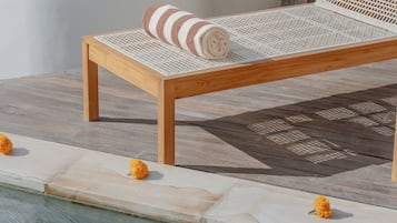 A wooden lounge chair with a white woven seat and backrest, positioned next to a pool with a tiled edge.