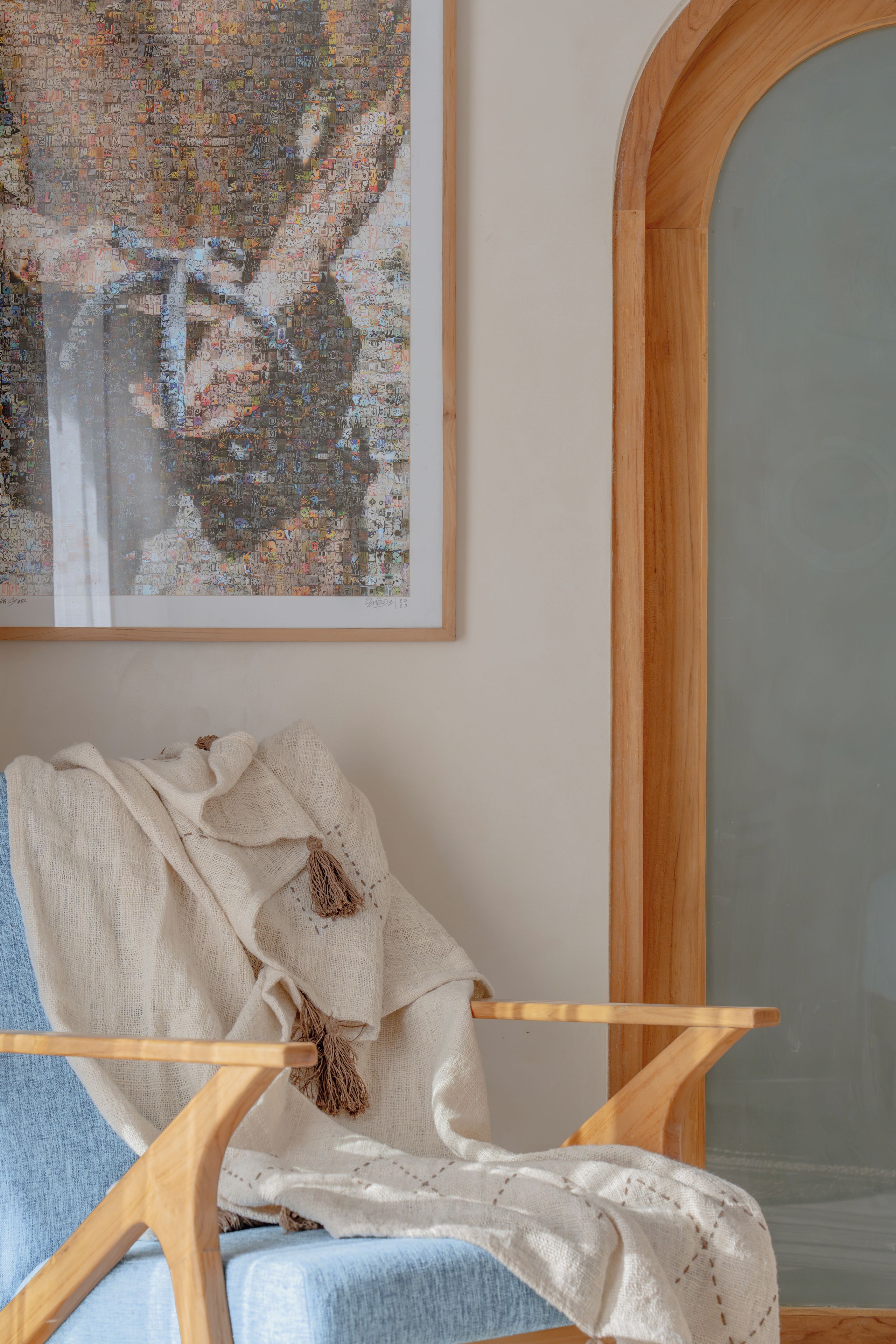 Een kamer met een stoel met houten frame, een witte deken en een groot abstract schilderij aan de muur.