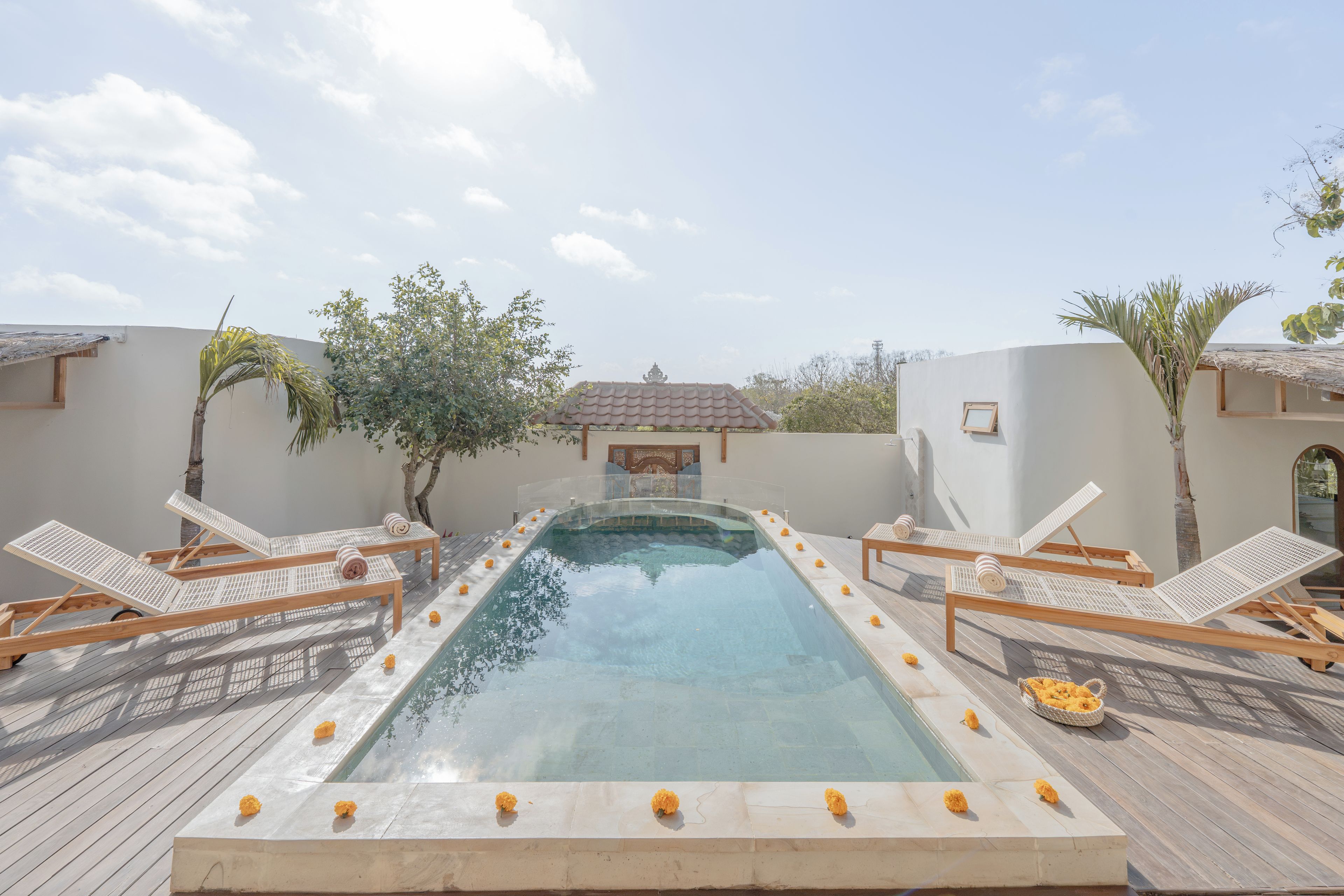A rectangular swimming pool with a clear blue water surface, surrounded by wooden lounge chairs with white cushions and a wooden deck.