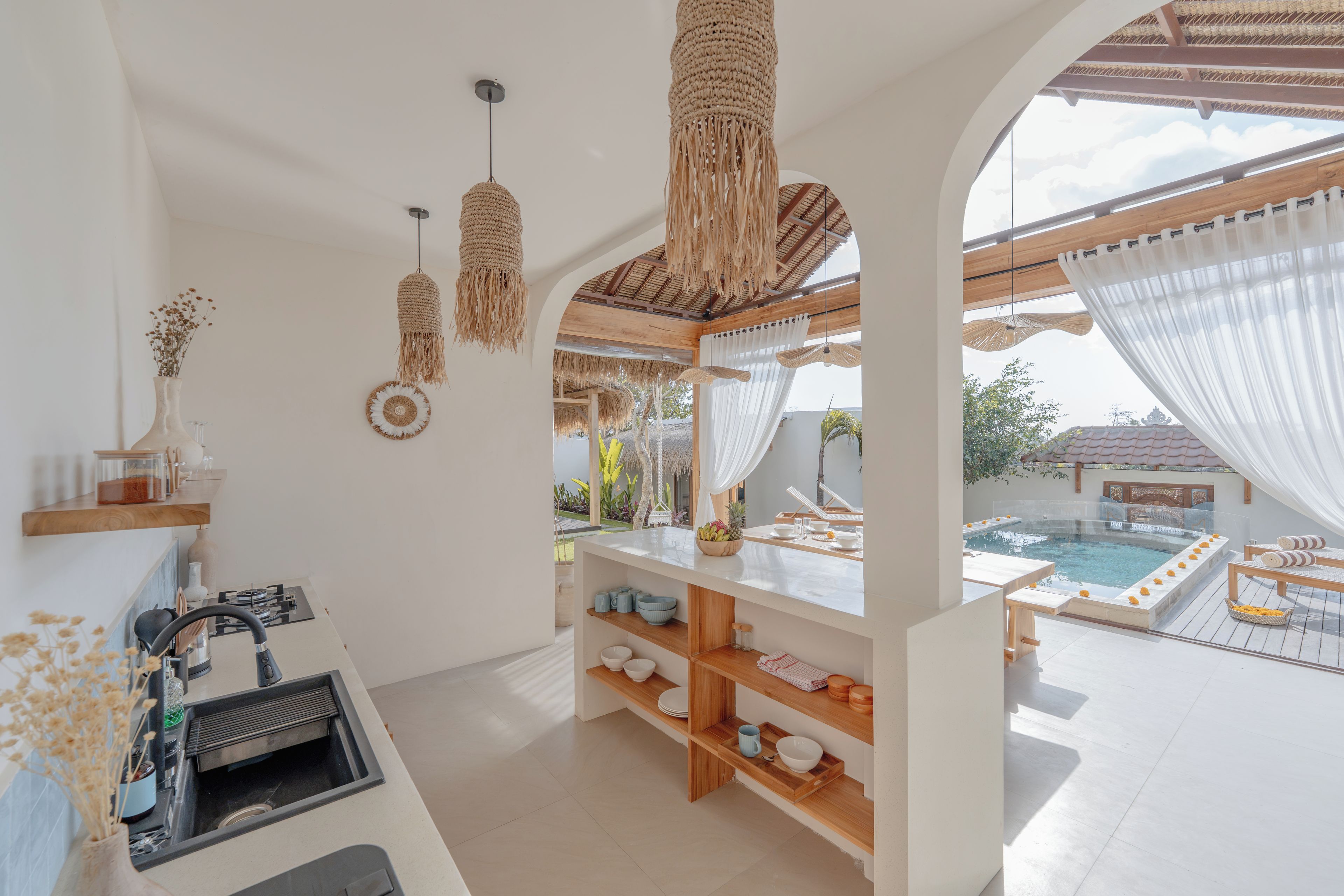 Een moderne keuken met een inbouwspoelbak, houten planken en uitzicht op een buitenzwembad.