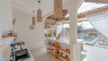 Una cocina moderna con pileta integrada, estantes de madera y vista a un área de piscina exterior.