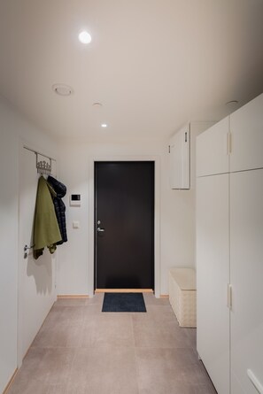 A hallway with a dark door, a coat rack with jackets, and a small bench. - Modern Apartment in Tromsø Center (Tromsø)