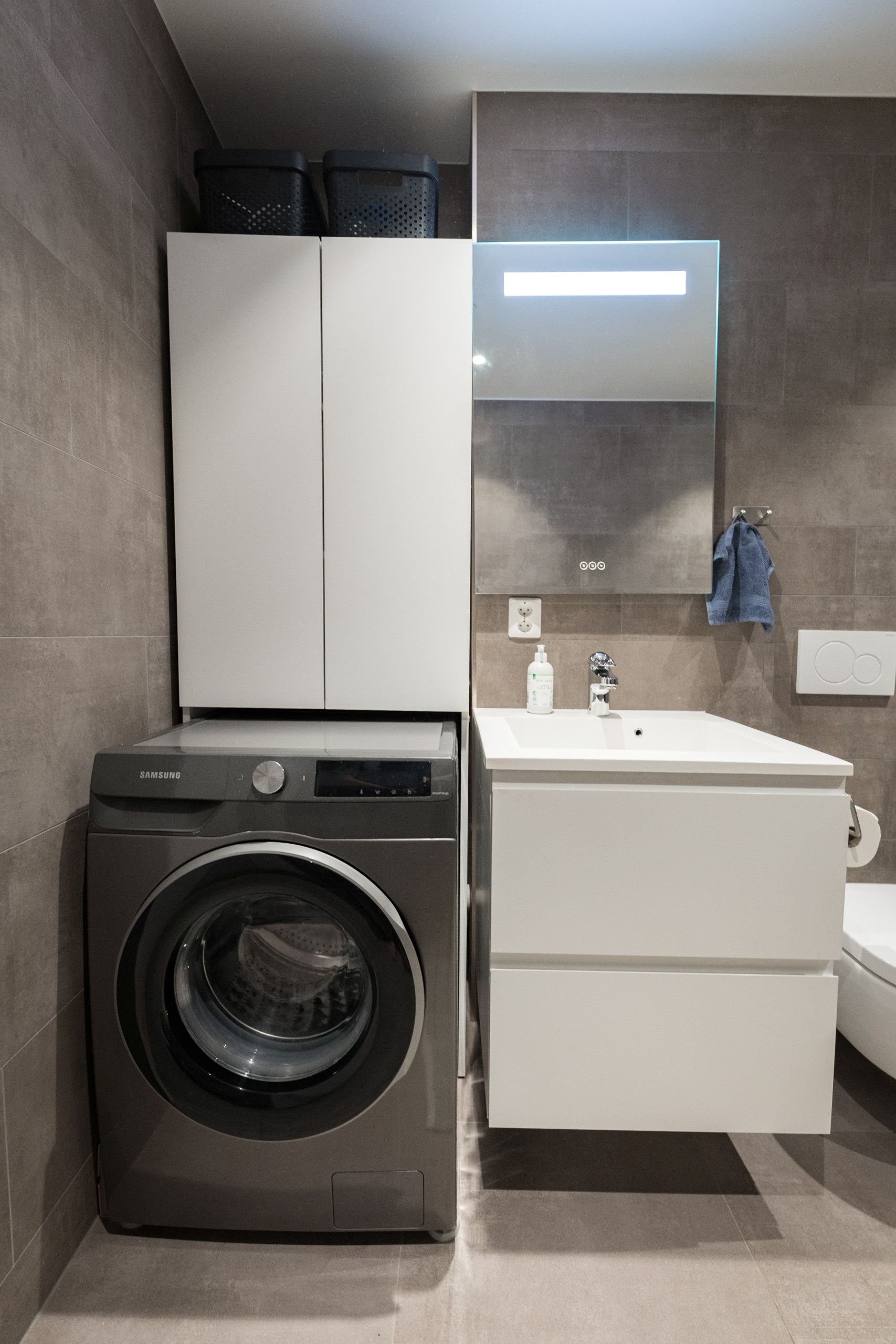 Ein kleines Badezimmer mit Waschmaschine, Waschbecken und Spiegel.