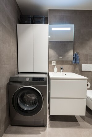 Un baño pequeño con lavadora, lavamanos y espejo.