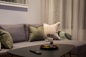 A modern living room with a grey sofa, multiple cushions, a small table with a remote control, and a window with curtains. - Modern Apartment in Tromsø Center (Tromsø)