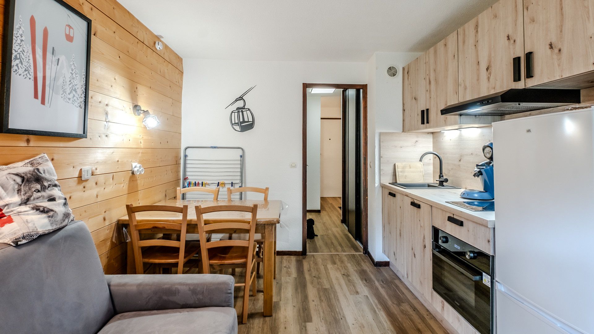 A compact kitchen with wooden cabinets, a dining area with a table and chairs, and a refrigerator.