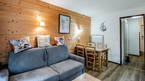 Ein Zimmer mit einer Holzwand, einem grauen Sofa mit gemusterten Kissen, einem Holzesstisch mit Stühlen und einem gerahmten Bild über dem Sofa.