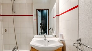 Ein Badezimmer mit weißem Waschbecken, einem Spiegel, einer Dusche und einem roten Streifen an der Wand.