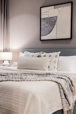 A neatly arranged bedroom with a bed, pillows, a blanket, a bedside table with a lamp, and a wall-mounted abstract artwork. - Bang Tao - King and Twin Comfort (Choeng Thale)