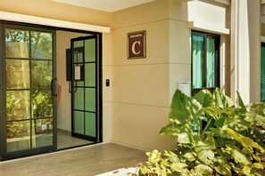 Une entrée d’immeuble avec une porte en verre, une enseigne indiquant « Bâtiment C » et une plante en pot.