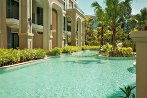 A swimming pool with a curved design, surrounded by lush greenery and a multi-story building with arched windows. - Bang Tao - King and Twin Comfort (Choeng Thale)