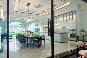 Un hall d’hôtel moderne avec une cloison en verre, un coin repas avec une table dressée pour deux personnes et un espace cuisine doté d’un plan de travail en marbre.