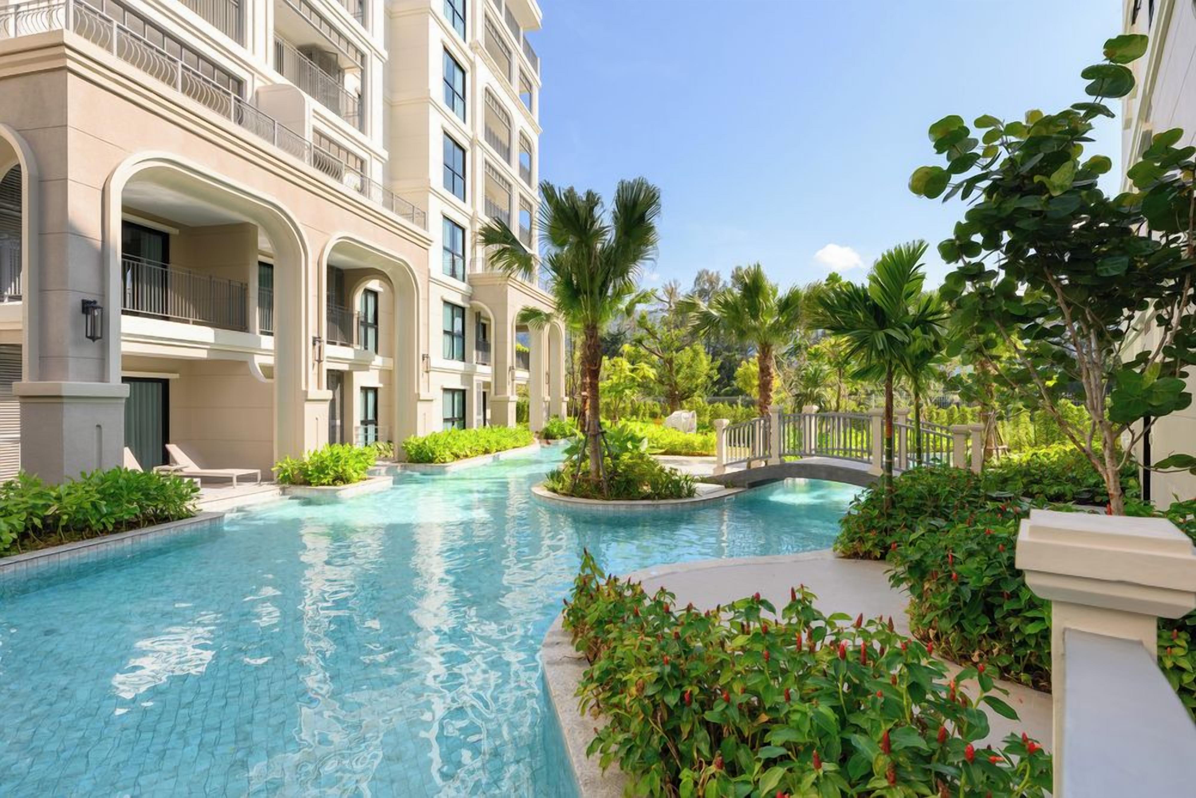 A swimming pool surrounded by lush greenery and a multi-story building with balconies.