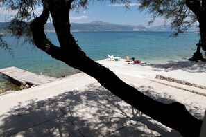 Ein klarer Blick auf einen See mit einem hölzernen Steg, der zu einem Strand mit Liegestühlen und einer kleinen Statue führt.